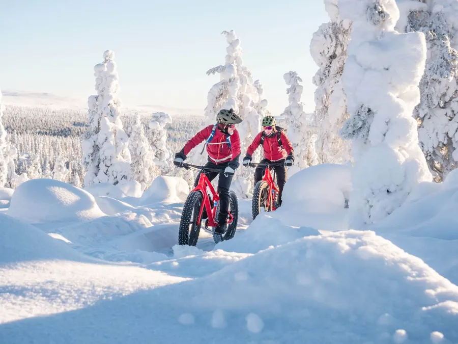 Dos ciclistas en un sendero nevado entre árboles