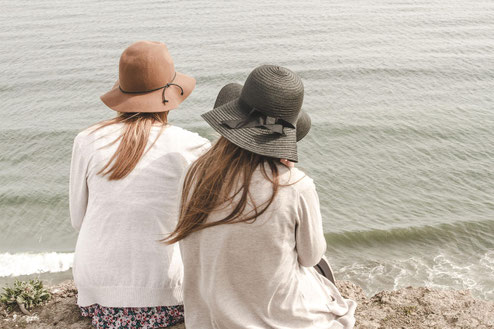 Zwei Frauen mit Hüten sitzen am Wasser