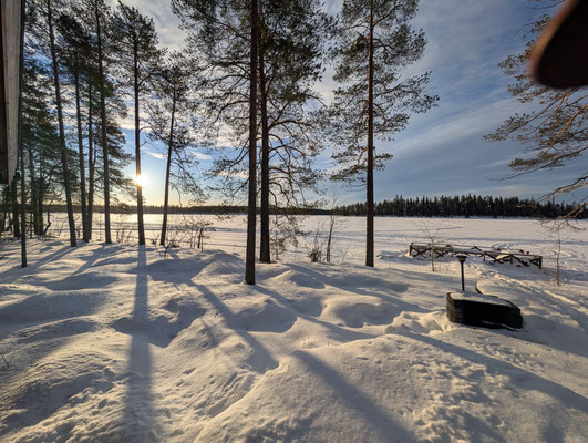 Sonnenlicht und Baumschatten auf dem verschneiten Seeufer