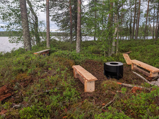 Holzbänke und Feuerstelle zwischen Bäumen am See