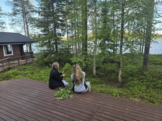 Zwei Personen sitzen auf der Holzterrasse zwischen Birken