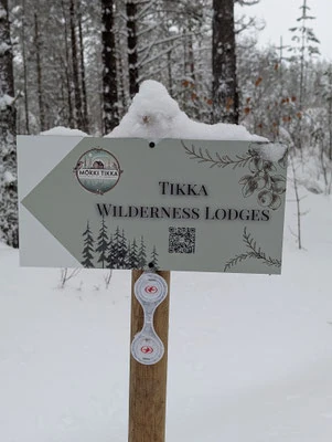 Verschneites Wegweiserschild von Tikka Wilderness Lodges im Wald