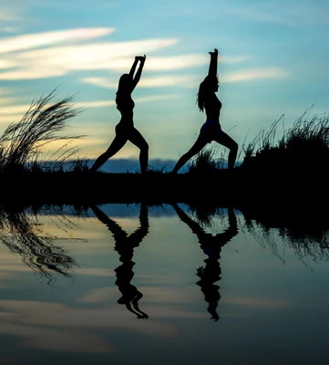 Silhouetten zweier Personen bei Yogaübungen am Wasser