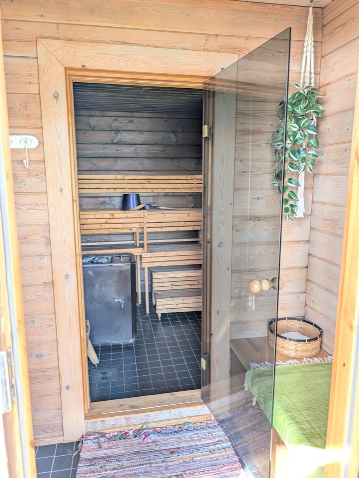 Offene Glastür zur Sauna mit Holzbänken und Birkenbesen